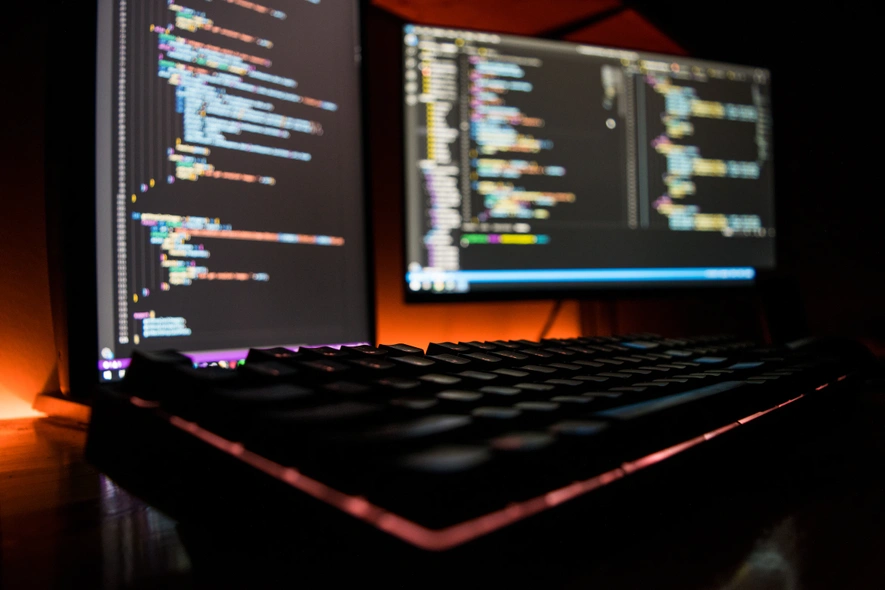 A keyboard and two monitors showing blurred lines of code, such as might be required for software package management.